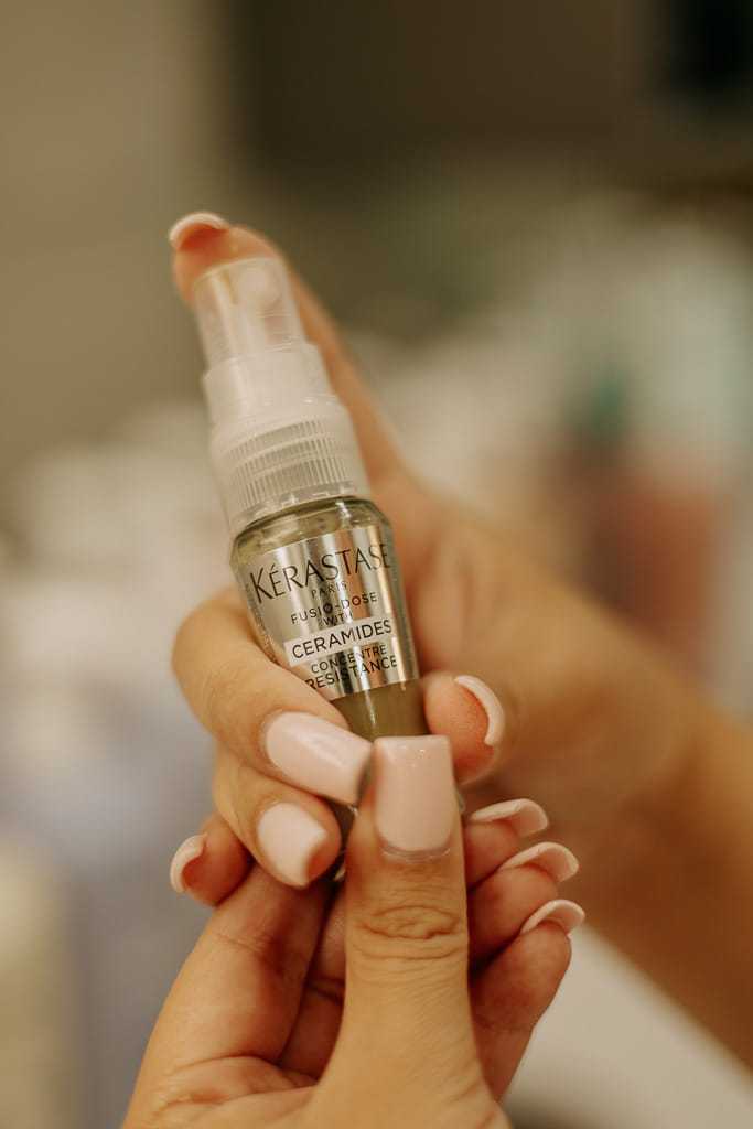Hands holding a small spray bottle labeled "Kérastase" in a close-up view.