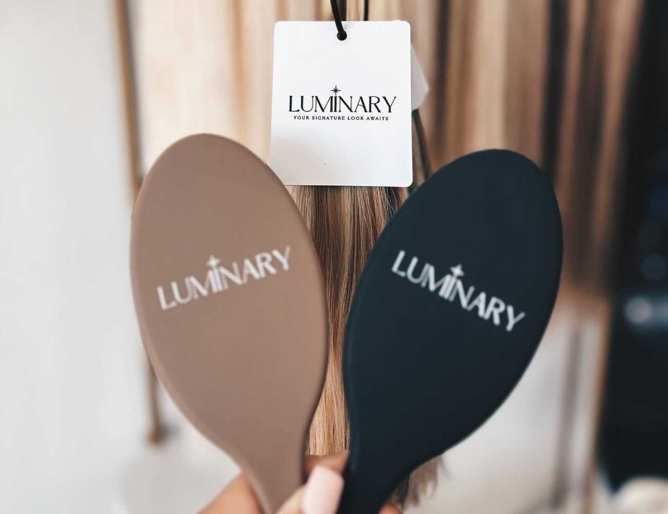 Two brushes with "Luminary" logo, displayed in front of hair strands.