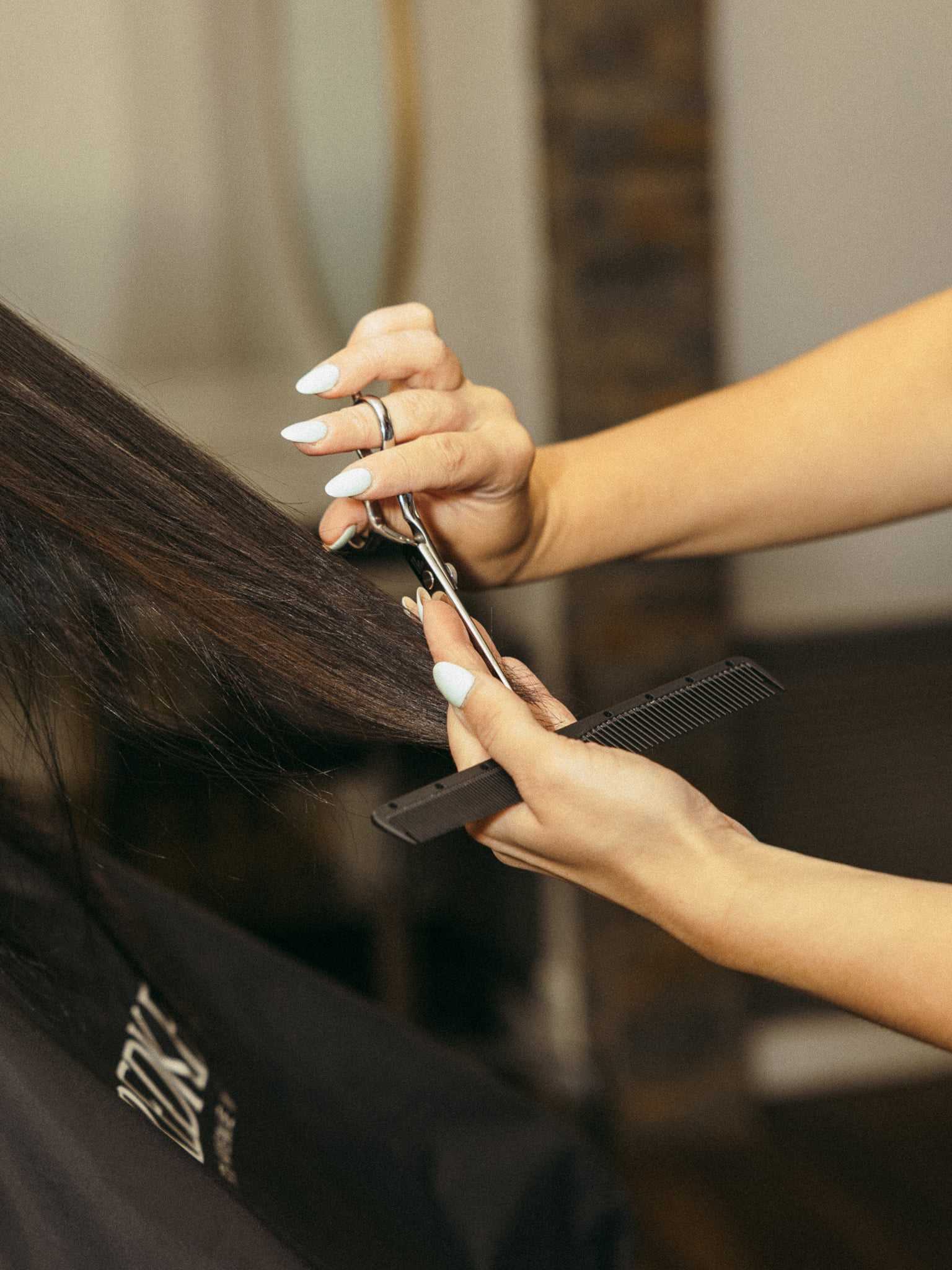 Hairdresser trims long, straight hair with scissors and a comb. Close-up of hands in a salon setting.