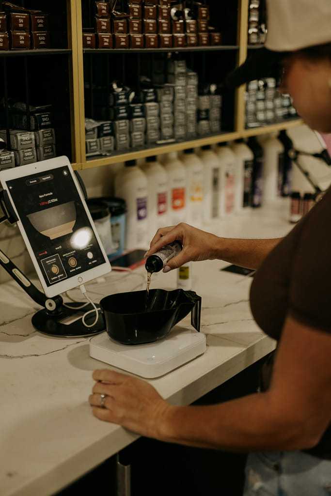 A person pouring liquid into a bowl on a scale, with a tablet displaying product info nearby.