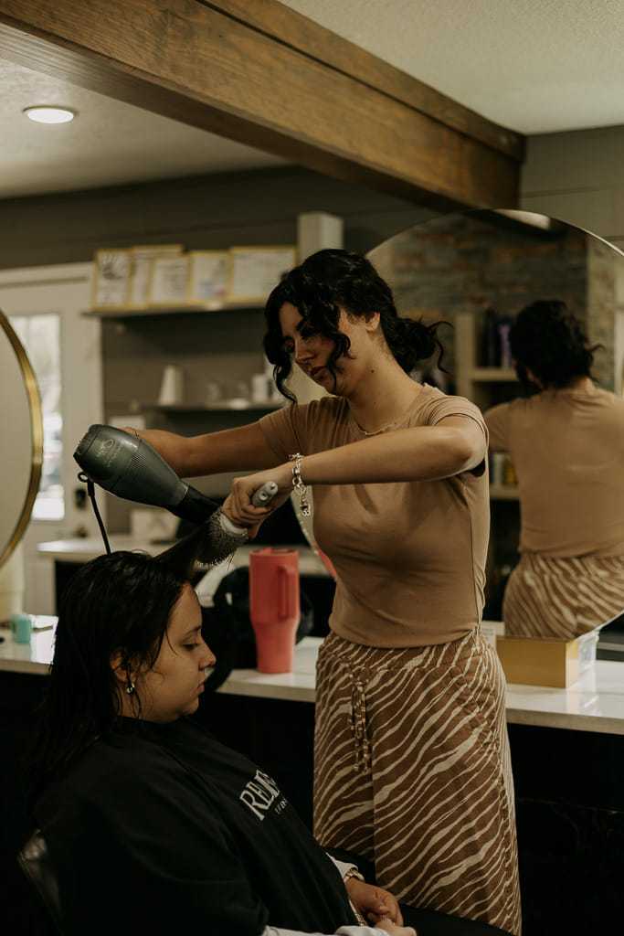 Hairdresser blow-drying client's hair in a modern salon.