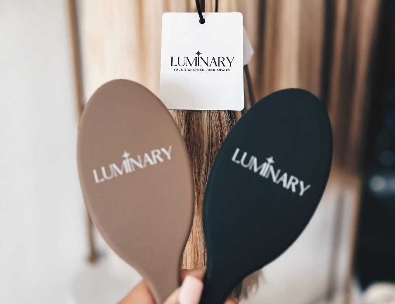 Two brushes with "Luminary" logo, displayed in front of hair strands.