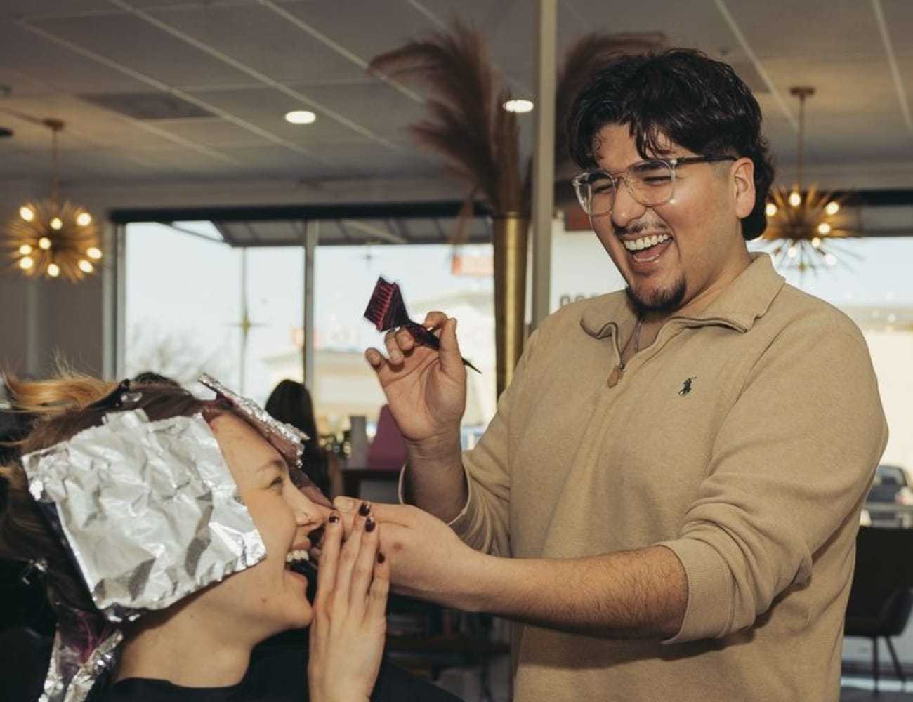 Hairdresser laughing with client during hair coloring session in a modern salon.